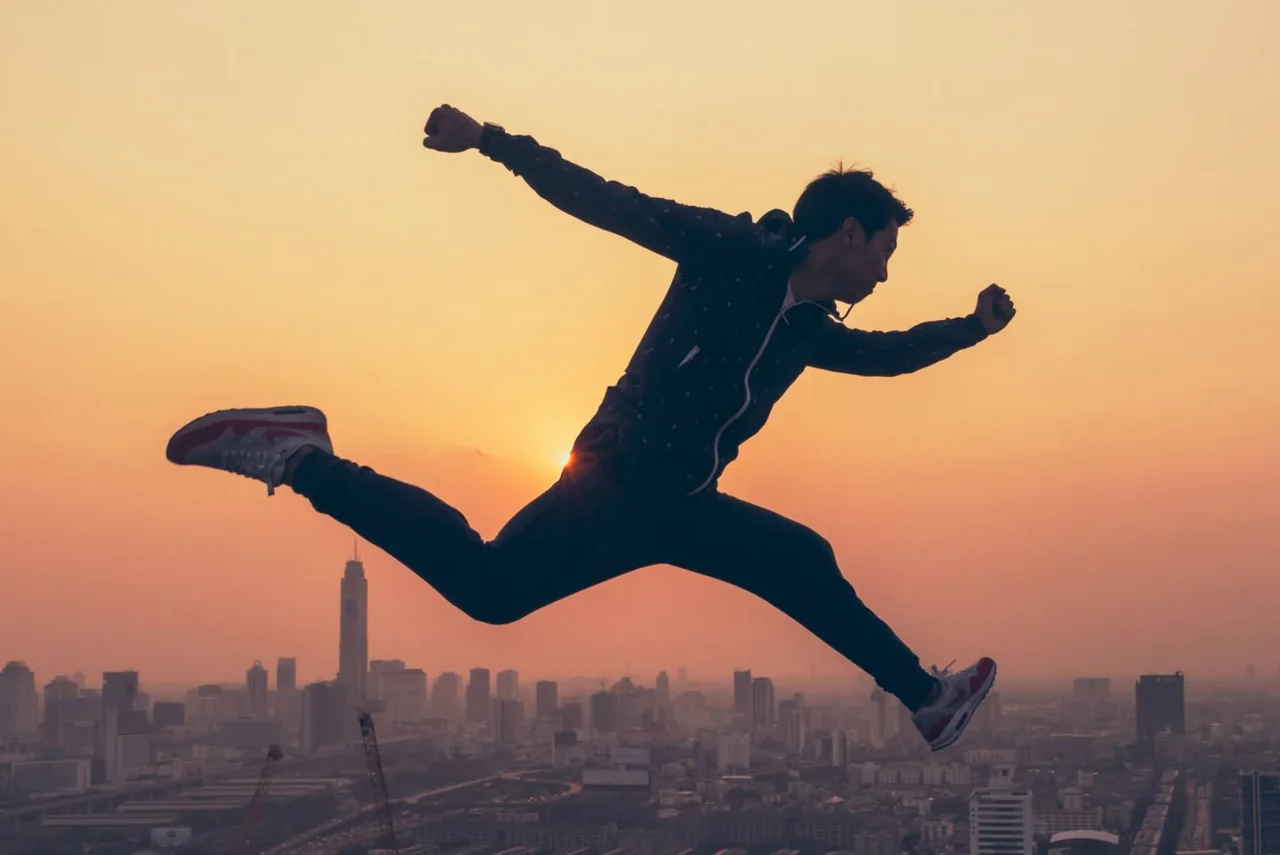 A silhouetted figure leaps across a golden city skyline.