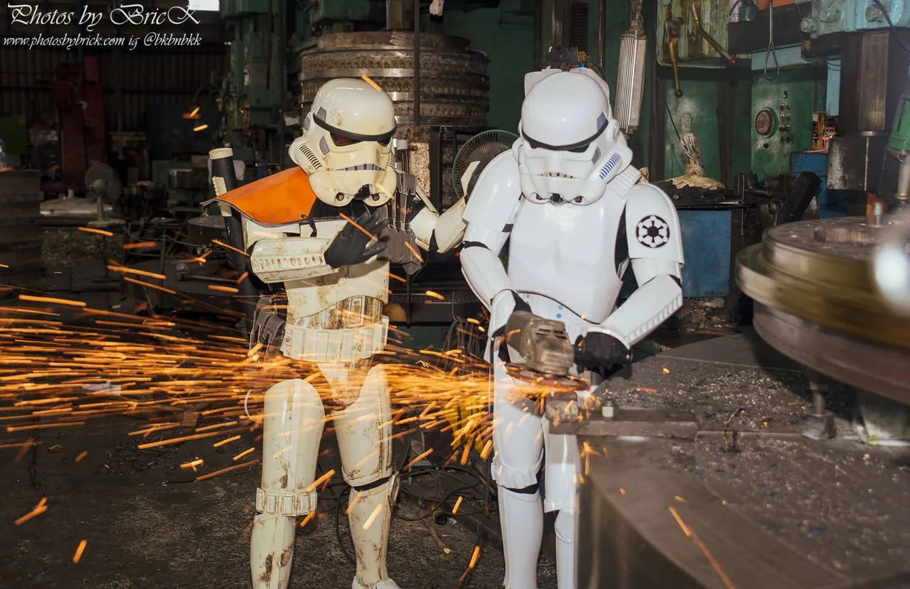Two white-armored costume characters beside sparks in a workshop.