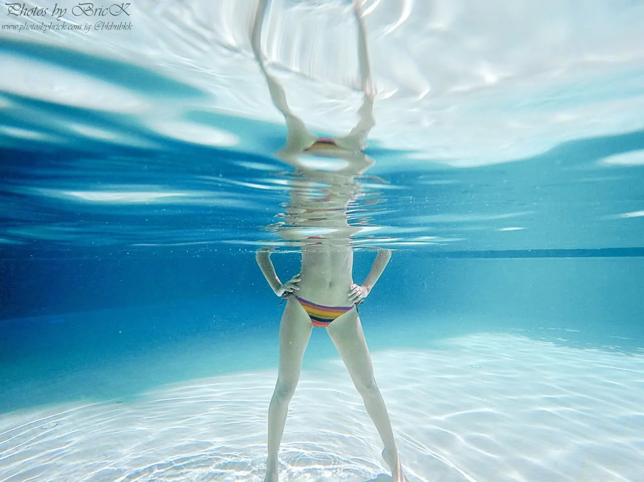 An underwater figure and a wavering reflection in turquoise water.