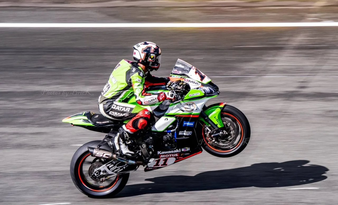 A green motorcycle lifts its front wheel against a blurred track.