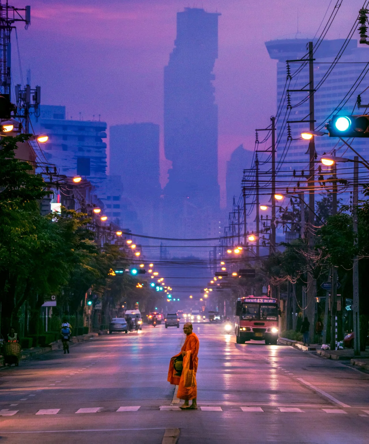 A person in orange robes walks across a purple twilight street.