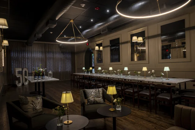 A long dining table and warm lamps beneath curved ceiling lights in a restaurant.