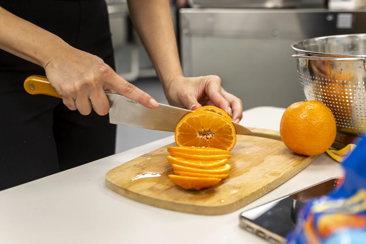 Hands slice a bright orange on a kitchen cutting board.