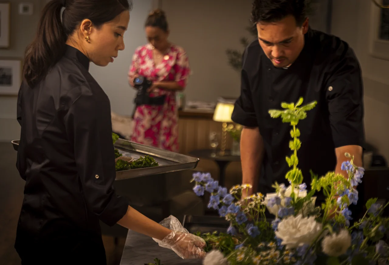 Restaurant staff prepare a table with plates, flowers and warm lamps.