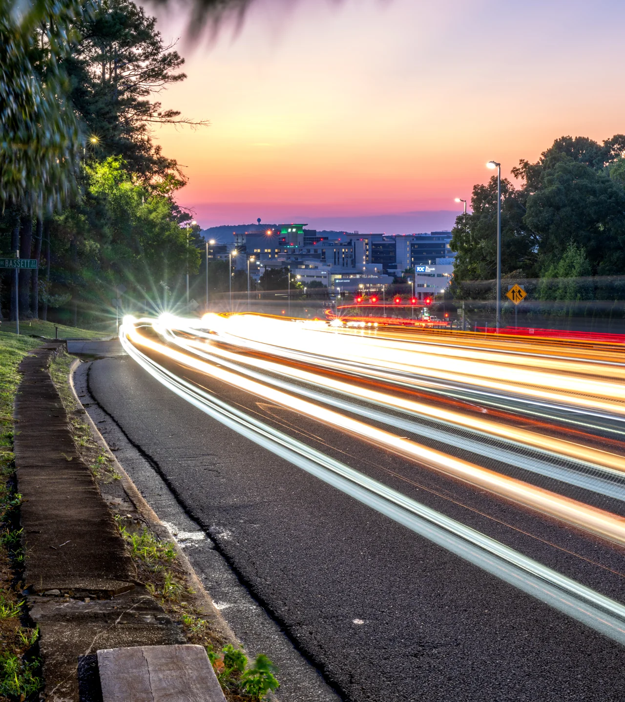 White light trails sweep downhill beneath a pink and orange evening sky.