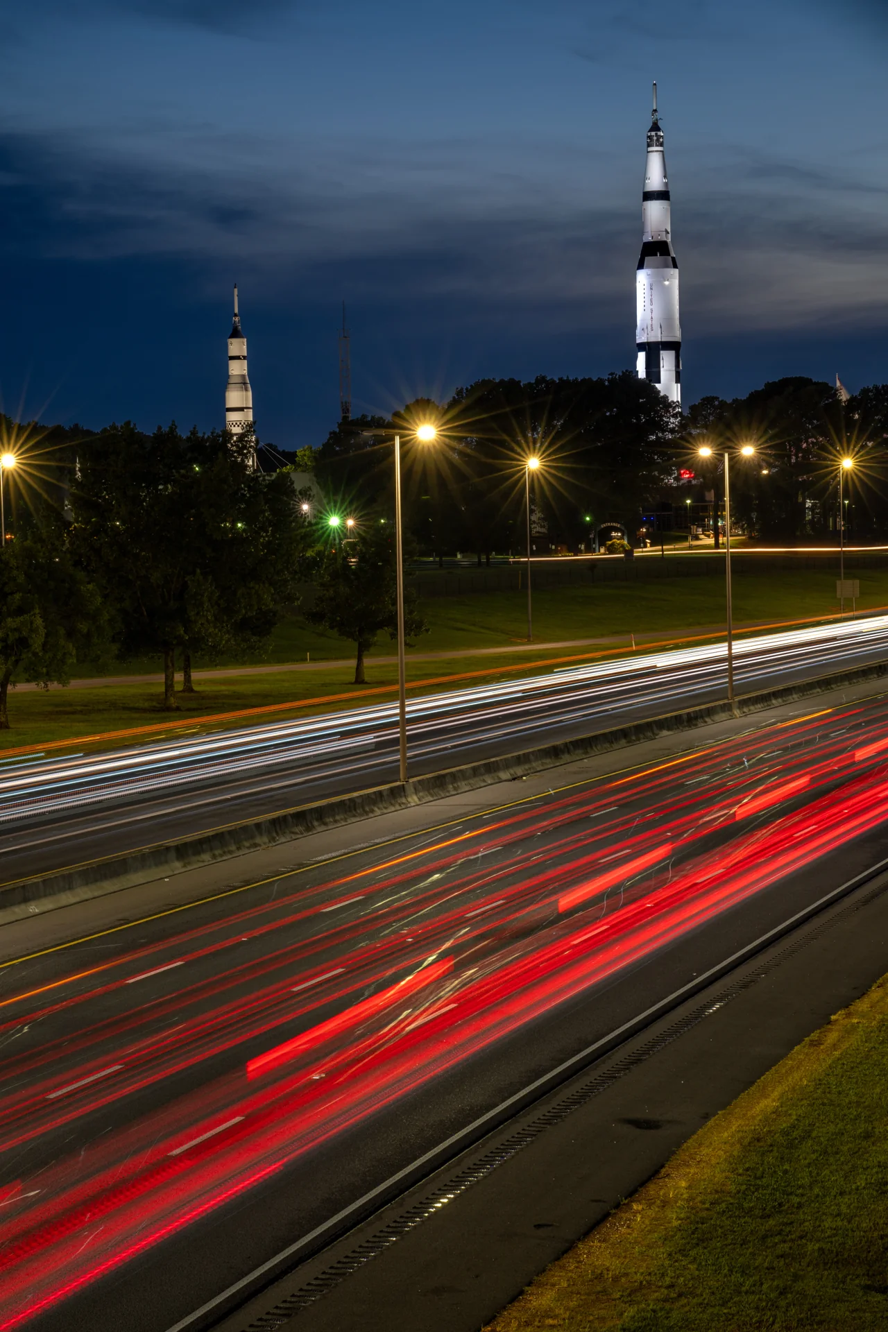 A vertical view of traffic trails leading toward an illuminated rocket-shaped landmark.