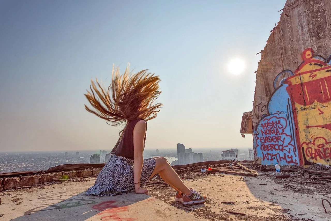 A woman whips her hair beside graffiti in warm outdoor light.