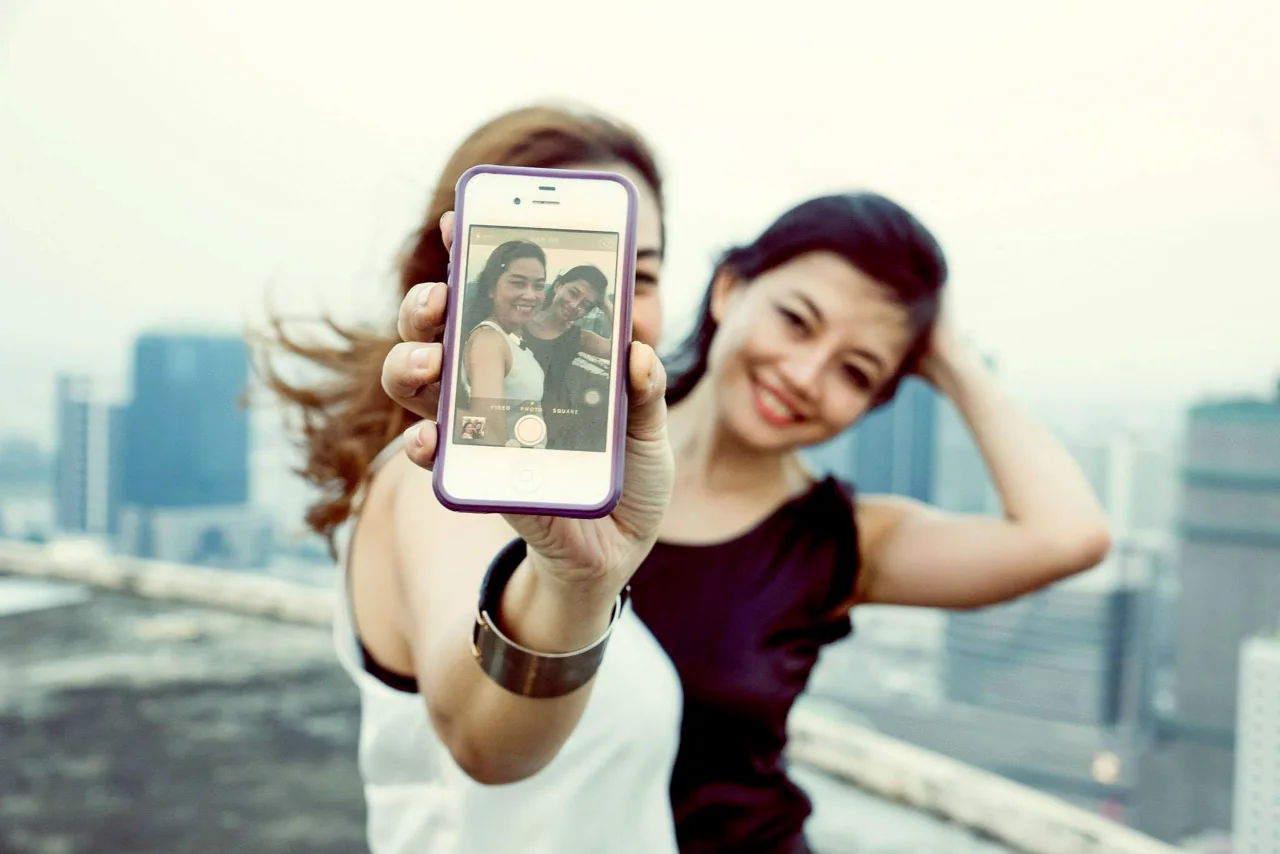 A woman looks at a phone with another person in the urban background.
