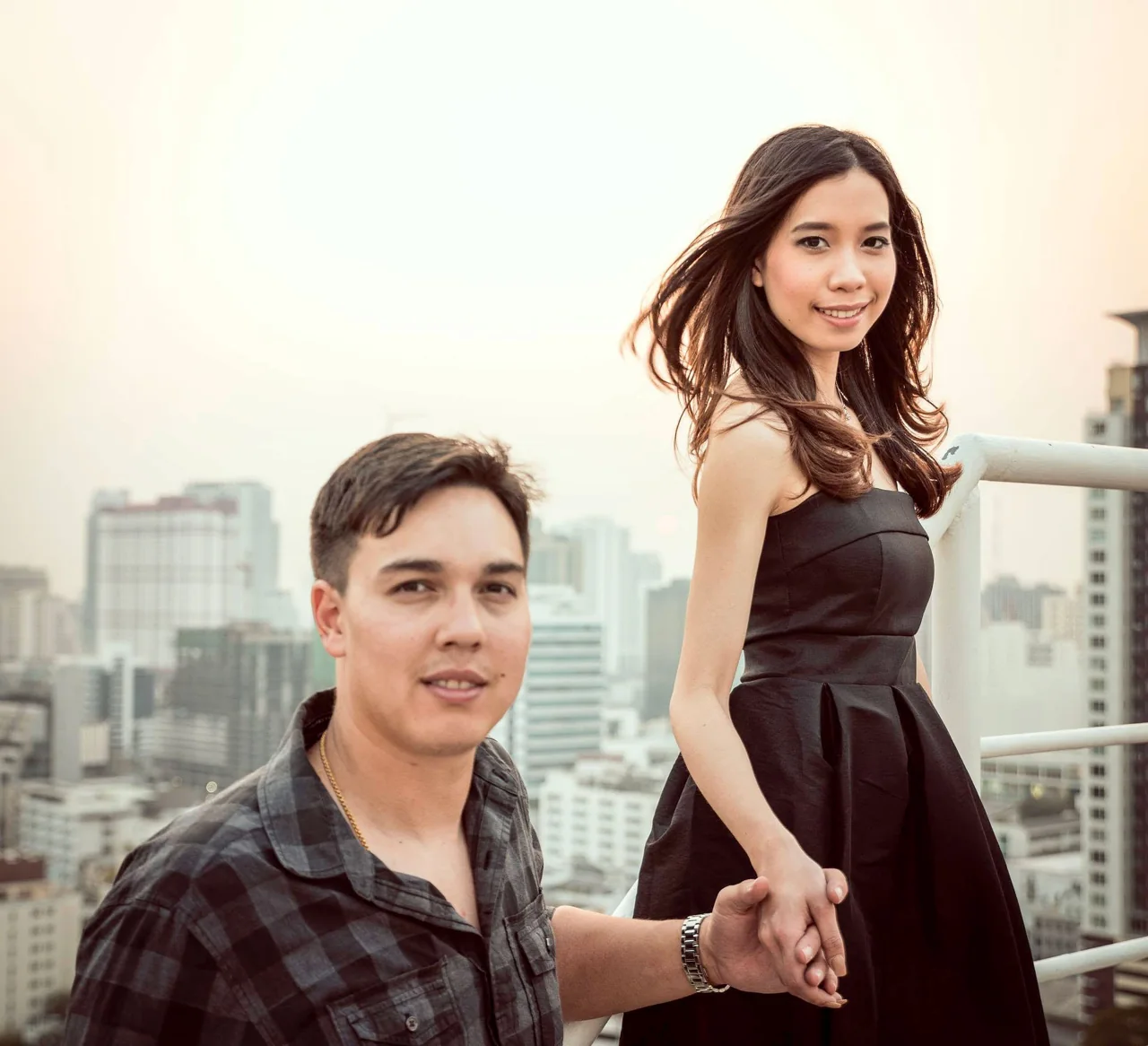 A formally dressed couple pose on an urban rooftop.