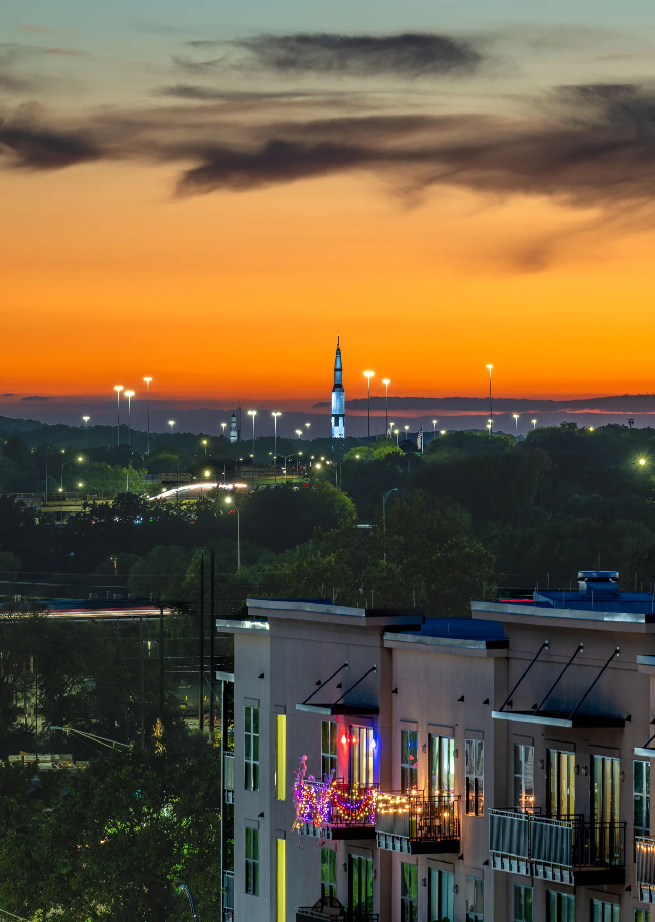 An orange evening sky stretches above rooftops and a distant illuminated landmark.